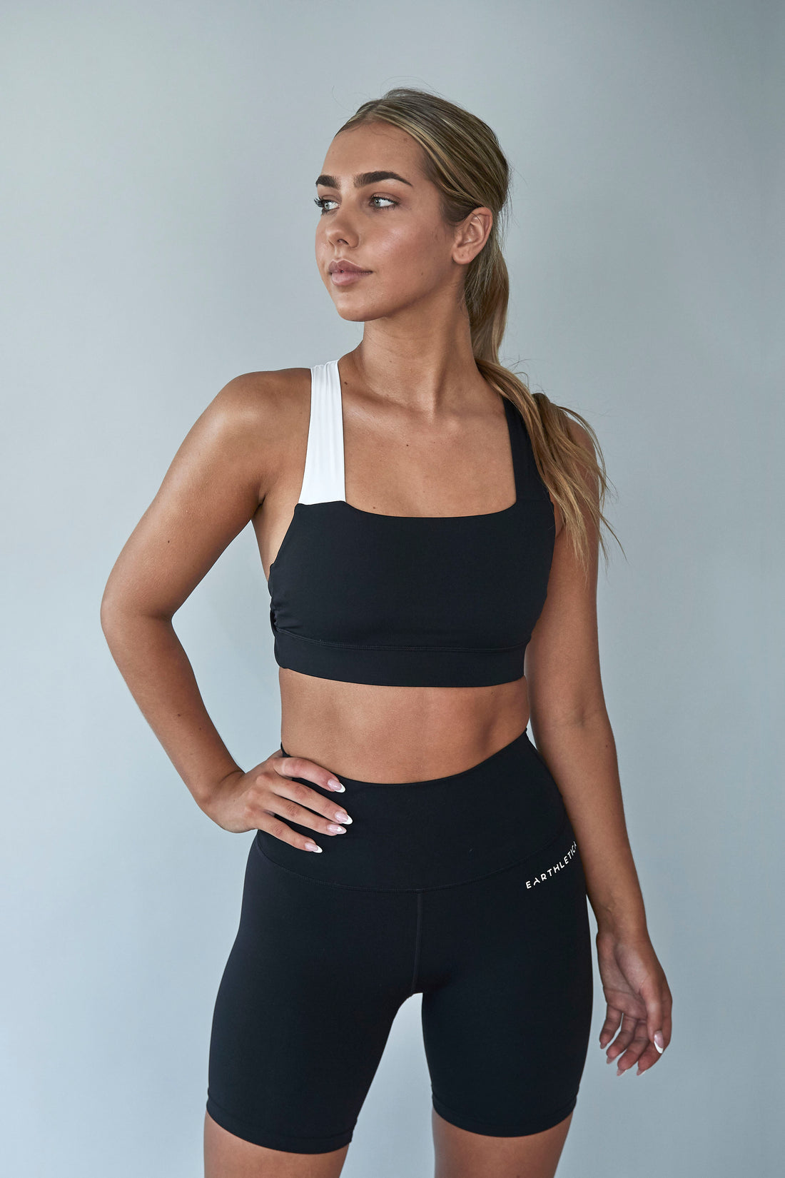 An Earthletica model wearing the Star Drop Crop + Midnight Bike Shorts activewear set. She is photographed from the front, with one hand on her hip.