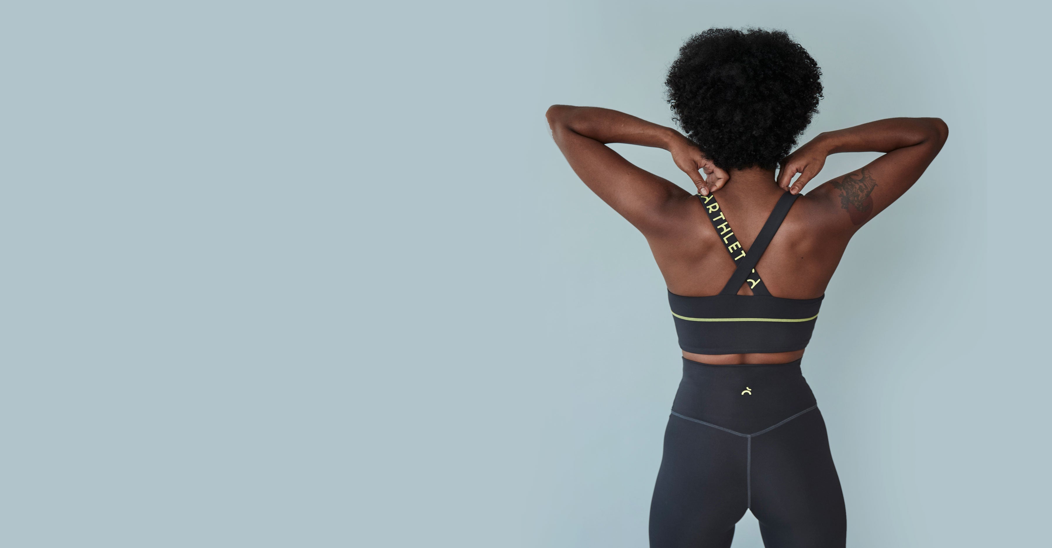 An Earthletica model wearing the Graphite Set. Her back is to the camera and she's adjusting the straps on her activewear crop.slider_item_FwFJED
