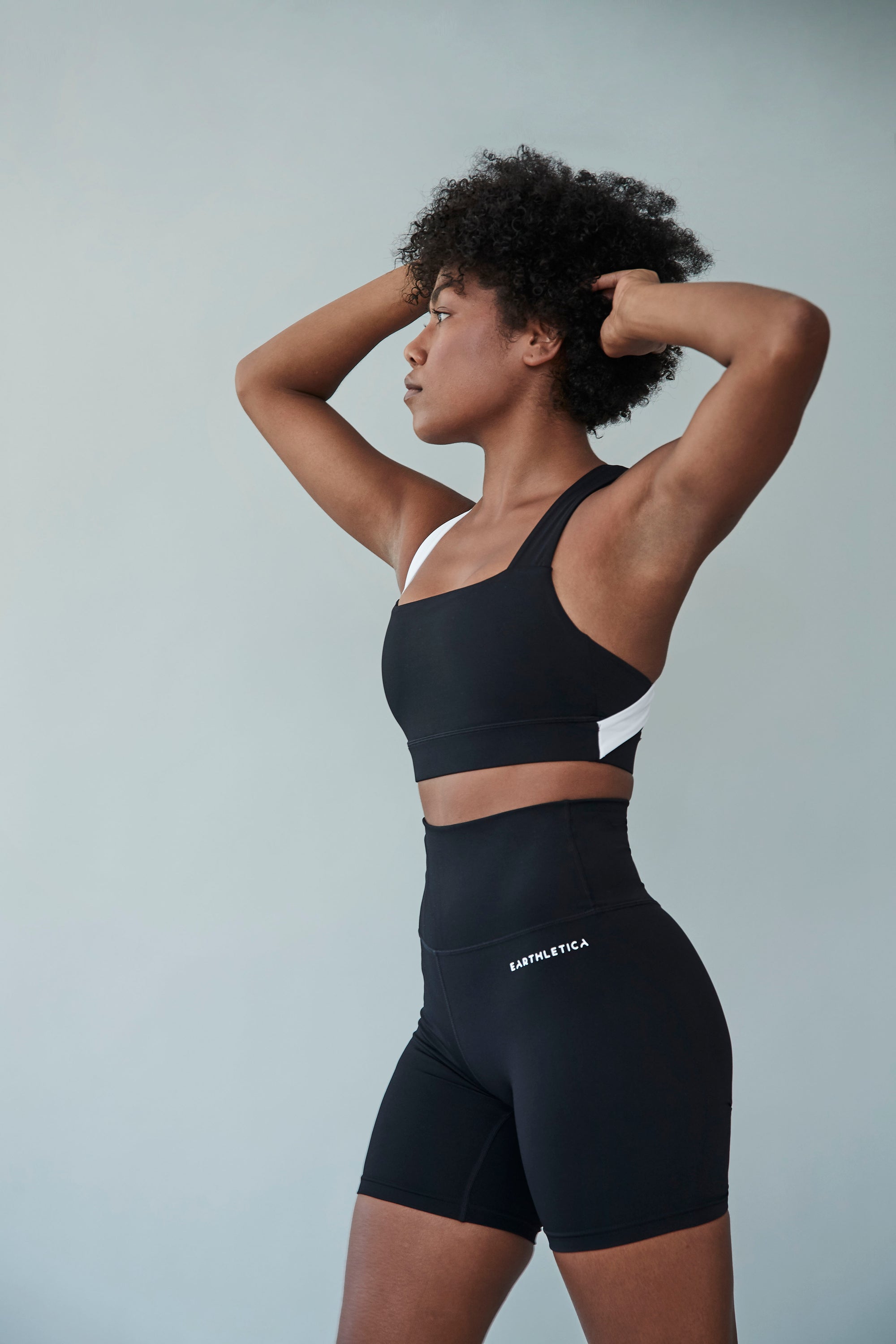 An Earthletica model wearing the Star Drop Crop + Midnight Bike Shorts activewear set. She is photographed from the front, with one hand on her hip.