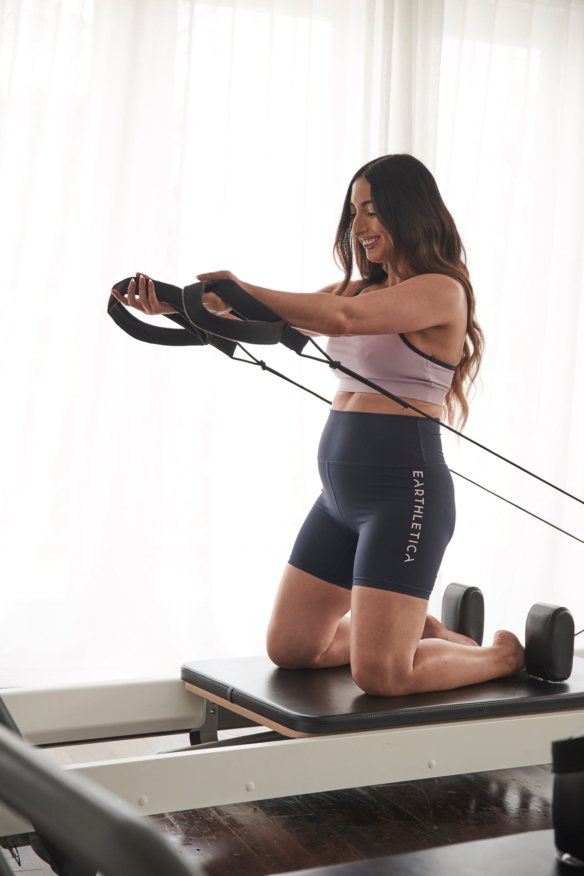 A pregnant Earthletica model, wearing the Beyond activewear set, on a pilates reformer