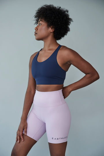 An Earthletica model wearing the Into The Blue crop and Lilac Dreaming bike shorts. She is turned to the right, gazing into the distance with a hand on her hip.