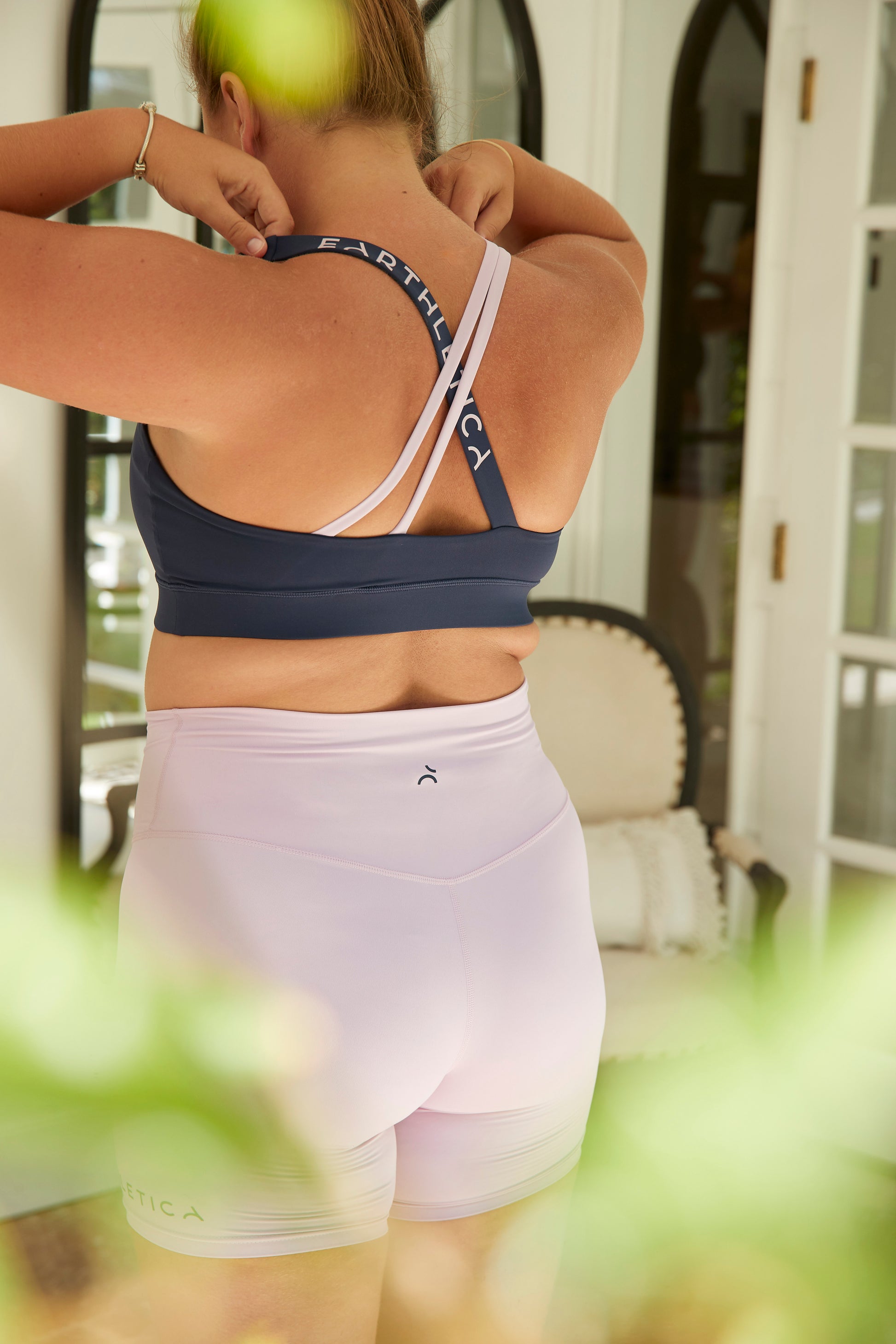 An Earthletica model wearing the Into The Blue crop and Lilac Dreaming bike shorts. She is photographed from behind while adjusting her crop.