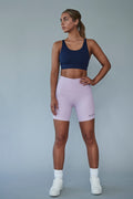 An Earthletica model wearing the Into The Blue crop and Lilac Dreaming bike shorts. She is turned to the right, gazing into the distance with a hand on her hip.