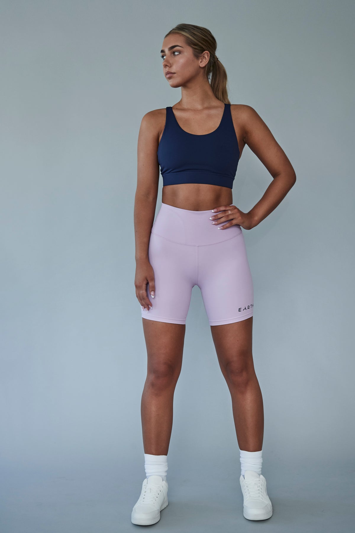 An Earthletica model wearing the Into The Blue crop and Lilac Dreaming bike shorts. She is turned to the right, gazing into the distance with a hand on her hip.