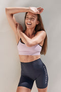 Earthletica Founder Libby Babet wearing the Beyond Set, standing against a white wall with her arm raised about her head and smiling